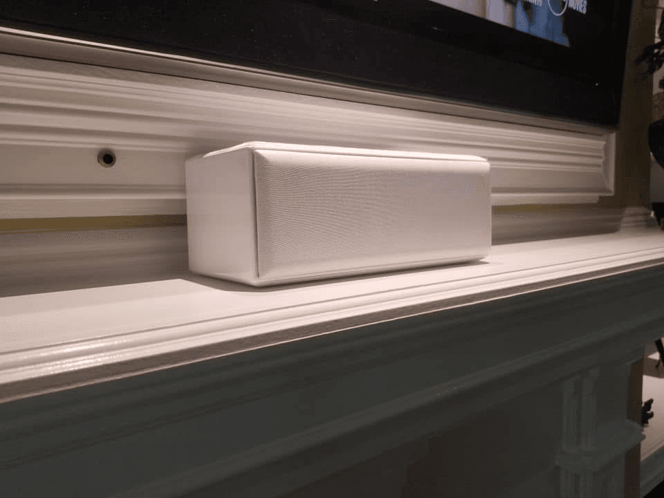 White center channel speaker on mantle shelf below wall-mounted TV