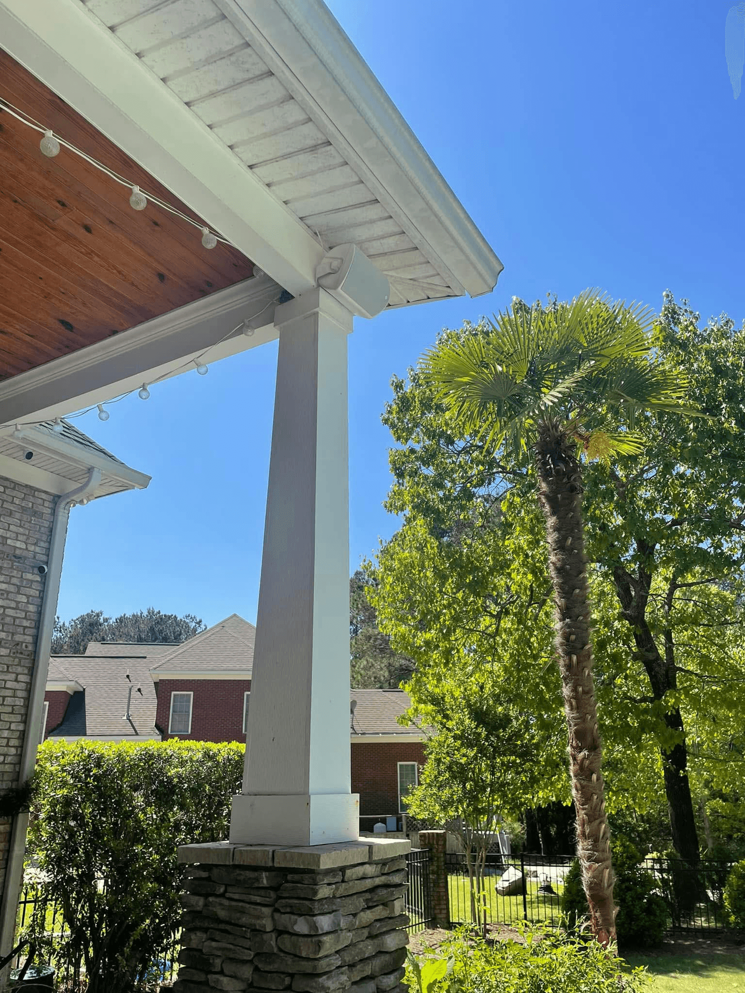 Covered porch with eave-mounted speakers, string lights, and stone column