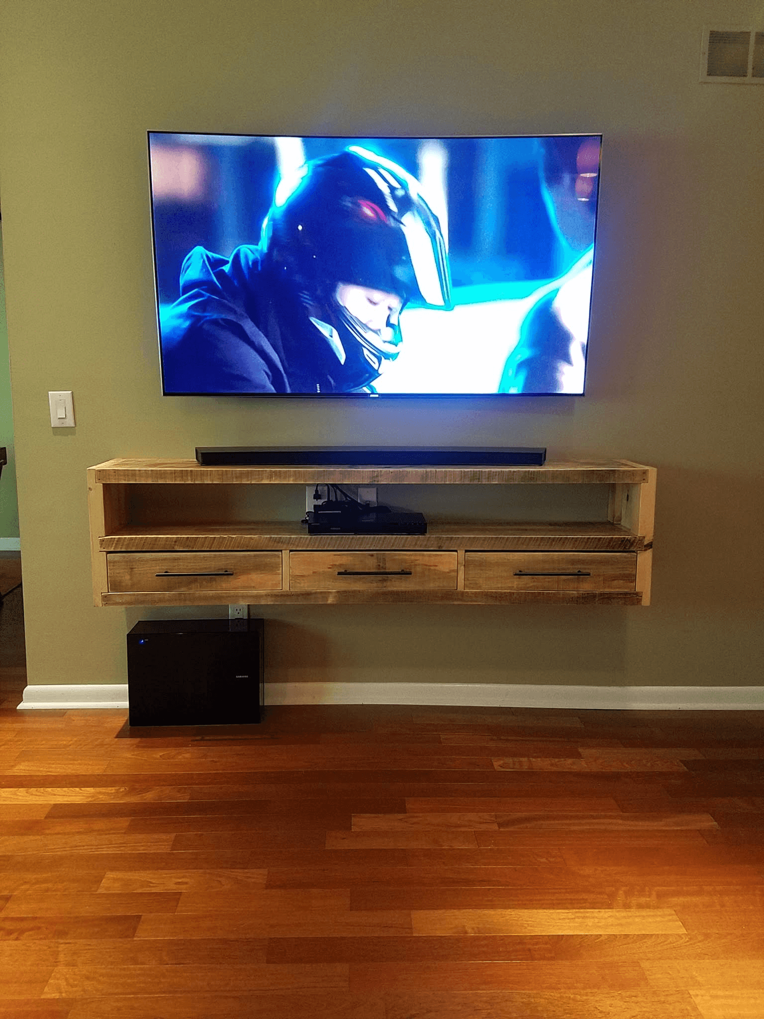 Curved TV wall-mounted above floating wood console with soundbar and subwoofer
