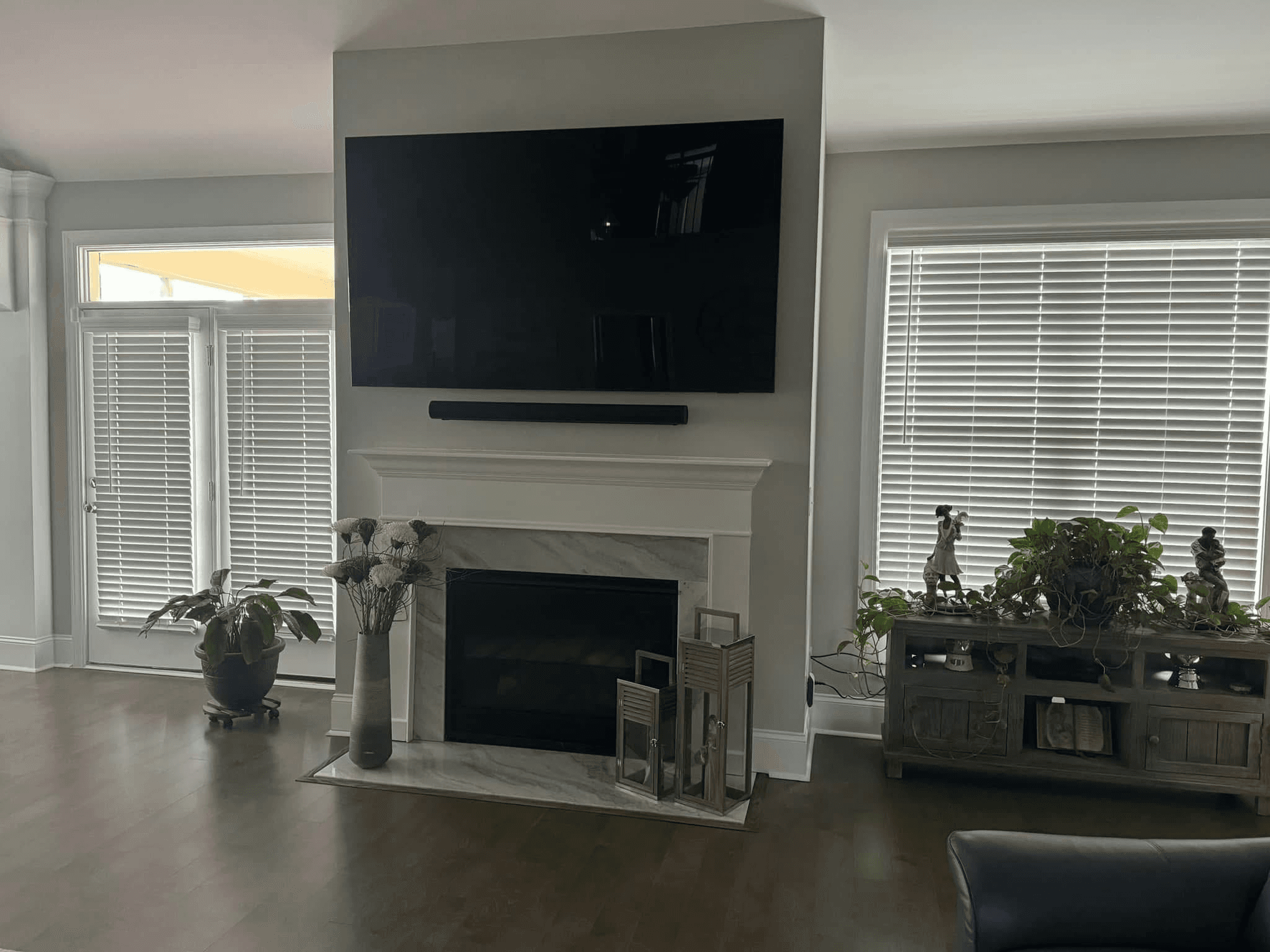 TV and soundbar mounted above white fireplace in living room with plants