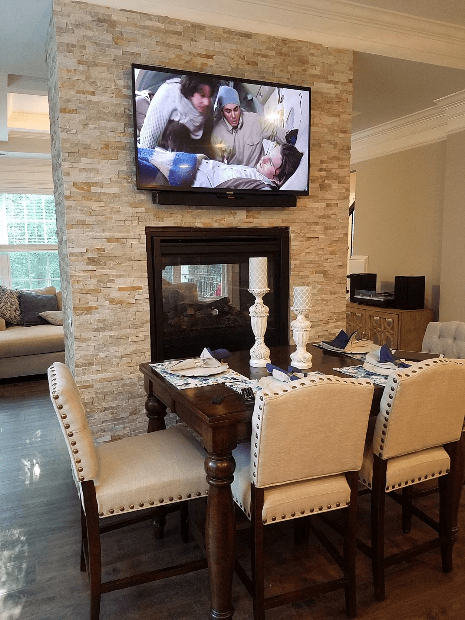 TV mounted on stacked stone two-sided fireplace wall in dining area