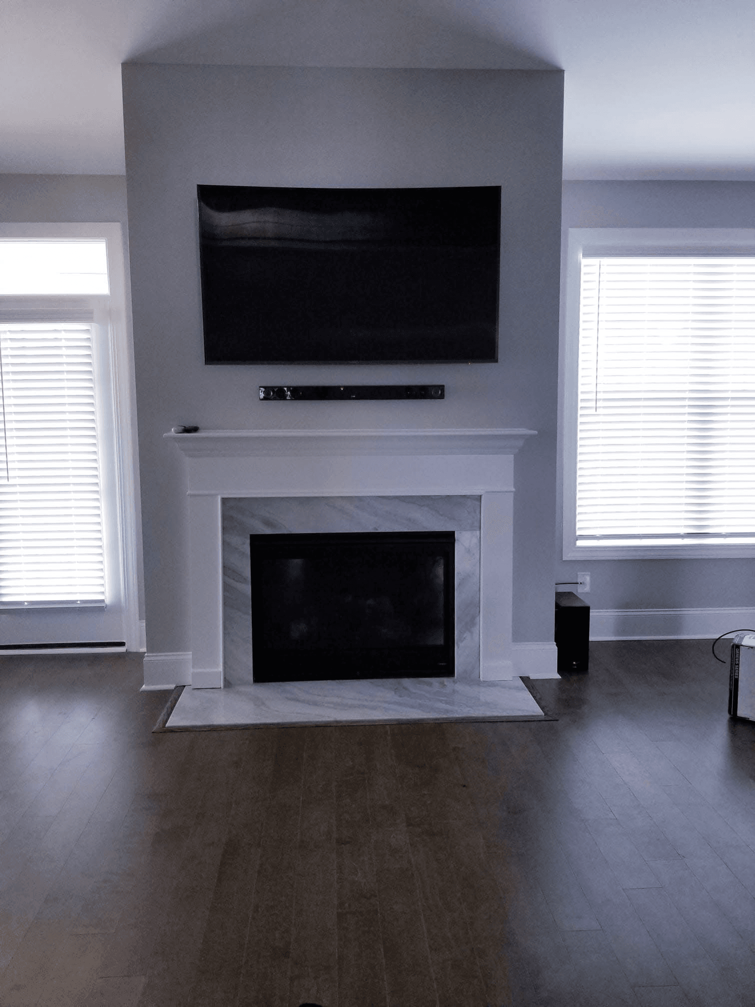 TV and soundbar mounted above modern gray fireplace with marble surround