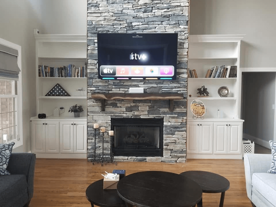 TV mounted on gray stone fireplace wall with Apple TV and built-in bookshelves